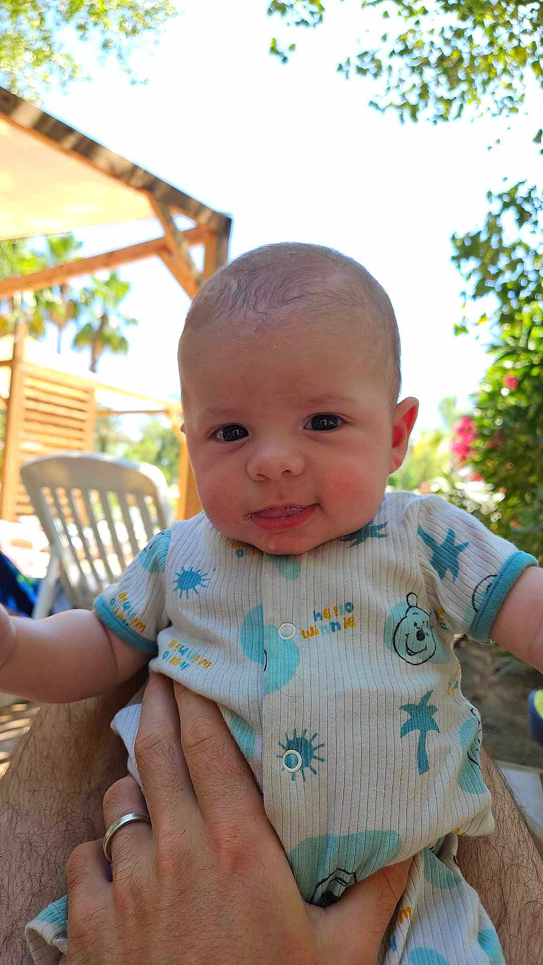 Nino a rejoint le concours — aidez-le/la à gagner de superbes lots ! baby, infant, child, person, outdoor, sunlight, greenery, clothing, onesie, hand, holding, face, smile, expression, nature, garden, chair, wood, daylight, cute
