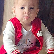 Nino participe au concours pour gagner de l'argent avec cette photo : toddler, child, face, red_jacket, white_shirt, cartoon_print, hands, glass_table, reflection, indoor, curious, pouty_expression, blond_hair, casual_clothing, young_child, person, portrait, sleeves, seated, home