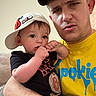 baby, child, man, indoor, casual_clothing, cap, necklace, holding, curious, serious_expression, portrait, people, person, close-up, skin, arm, facial_expression, sitting, couch, family