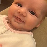 Madison is registered to the contest to win money with this photo: baby, smile, face, closeup, infant, eyes, tongue, clothing, pink_trim, white_outfit, soft_texture, skin, head, cheeks, person, young_child, cute, happy, indoors, resting