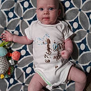 Maya joined the competition — help win amazing prizes! baby, infant, child, onesie, blanket, pattern, toy, hand, face, expression, wide_eyes, clenched_fist, floor, indoor, cute, skin, head, legs, foot, playful