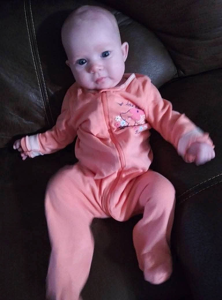 Maya is registered to the contest to win money with this photo: baby, blue_eyes, child, clothing, couch, cute, face, furniture, indoors, infant, leather, onesie, peach_color, person, portrait, relaxing, sitting, small, soft, young