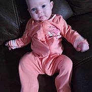Maya is registered to the contest to win money with this photo: baby, infant, onesie, peach_color, couch, leather, blue_eyes, face, person, child, sitting, indoors, cute, young, portrait, clothing, relaxing, furniture, soft, small