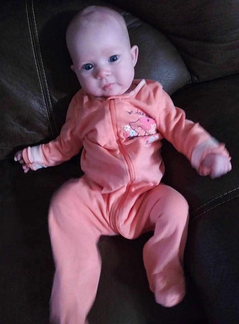 Maya is registered to the contest to win money with this photo: baby, infant, onesie, peach_color, couch, leather, blue_eyes, face, person, child, sitting, indoors, cute, young, portrait, clothing, relaxing, furniture, soft, small