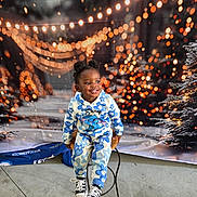 Se'Myra is registered to the contest to win money with this photo: child, smiling, sitting, stool, blue_flower_outfit, black_shoes, puffs_hairstyle, bokeh_lights, holiday_backdrop, pine_tree, indoor, concrete_floor, cute, happy, casual_clothing, portrait, decorative_lights, seasonal, festive, young
