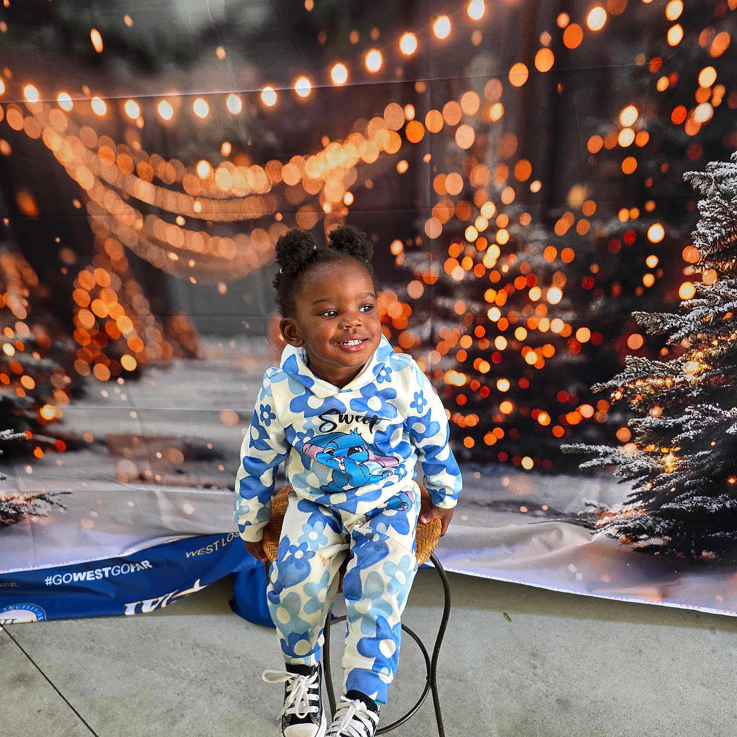 Se'Myra is registered to the contest to win money with this photo: black_shoes, blue_flower_outfit, bokeh_lights, casual_clothing, child, concrete_floor, cute, decorative_lights, festive, happy, holiday_backdrop, indoor, pine_tree, portrait, puffs_hairstyle, seasonal, sitting, smiling, stool, young