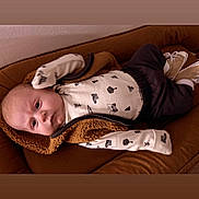 Elijah joined the competition — help win amazing prizes! baby, infant, child, couch, brown, clothing, vest, long_sleeve, pattern, footwear, shoes, indoor, person, face, expression, lying_down, furniture, cozy, soft, curious