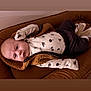 baby, infant, child, couch, brown, clothing, vest, long_sleeve, pattern, footwear, shoes, indoor, person, face, expression, lying_down, furniture, cozy, soft, curious