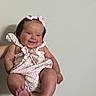 baby, infant, child, smile, pink_bow, romper, cute, happy, person, skin, face, arm, hand, foot, toes, indoor, wall, holding, portrait, head