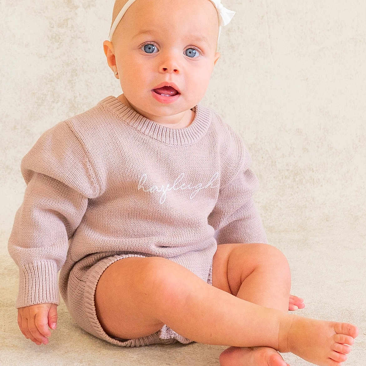 Hazeleigh is registered to the contest to win money with this photo: baby, blue_eyes, casual, child, cozy, cute, expression, foot, hand, headband, indoor, infant, knitwear, neutral_background, person, portrait, sitting, skin, sweater, young_child