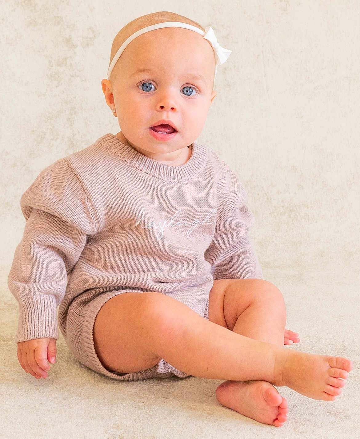 Hazeleigh is registered to the contest to win money with this photo: baby, child, blue_eyes, headband, knitwear, sweater, sitting, cute, indoor, portrait, skin, foot, hand, expression, neutral_background, young_child, person, infant, cozy, casual