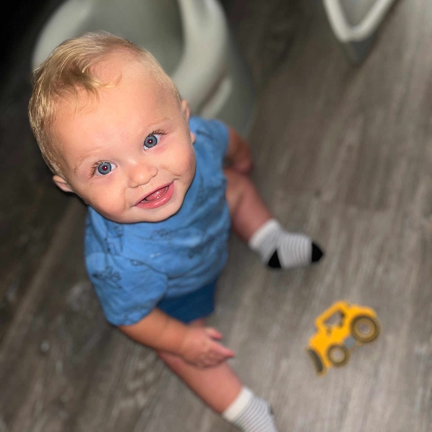 Aspen joined the competition — help win amazing prizes! baby, blond_hair, blue_eyes, blue_shirt, casual_clothing, child, cute, floor, happy, indoor, looking_up, person, playtime, sitting, small_toy, smiling, striped_socks, toddler, toy_truck, wooden_floor