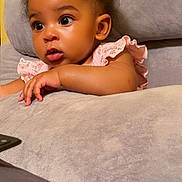 Emaan is registered to the contest to win money with this photo: baby, child, infant, curious, face, eyes, pink_clothing, floral_pattern, couch, soft_texture, yellow_wall, indoors, cute, portrait, skin, hair, hand, expression, seated, comfortable