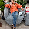child, girl, orange_hoodie, leopard_print_shoes, armchair, plant, smoothie, store, shopping, casual, jeans, indoor, relaxed, furniture, shopping_mall, people, flooring, bag, decor, person