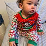 toddler, child, pajamas, christmas, holiday, striped, cushion, sitting, indoors, curly_hair, black_sock, hand, face, clothing, cute, young_child, person, portrait, seated, expression