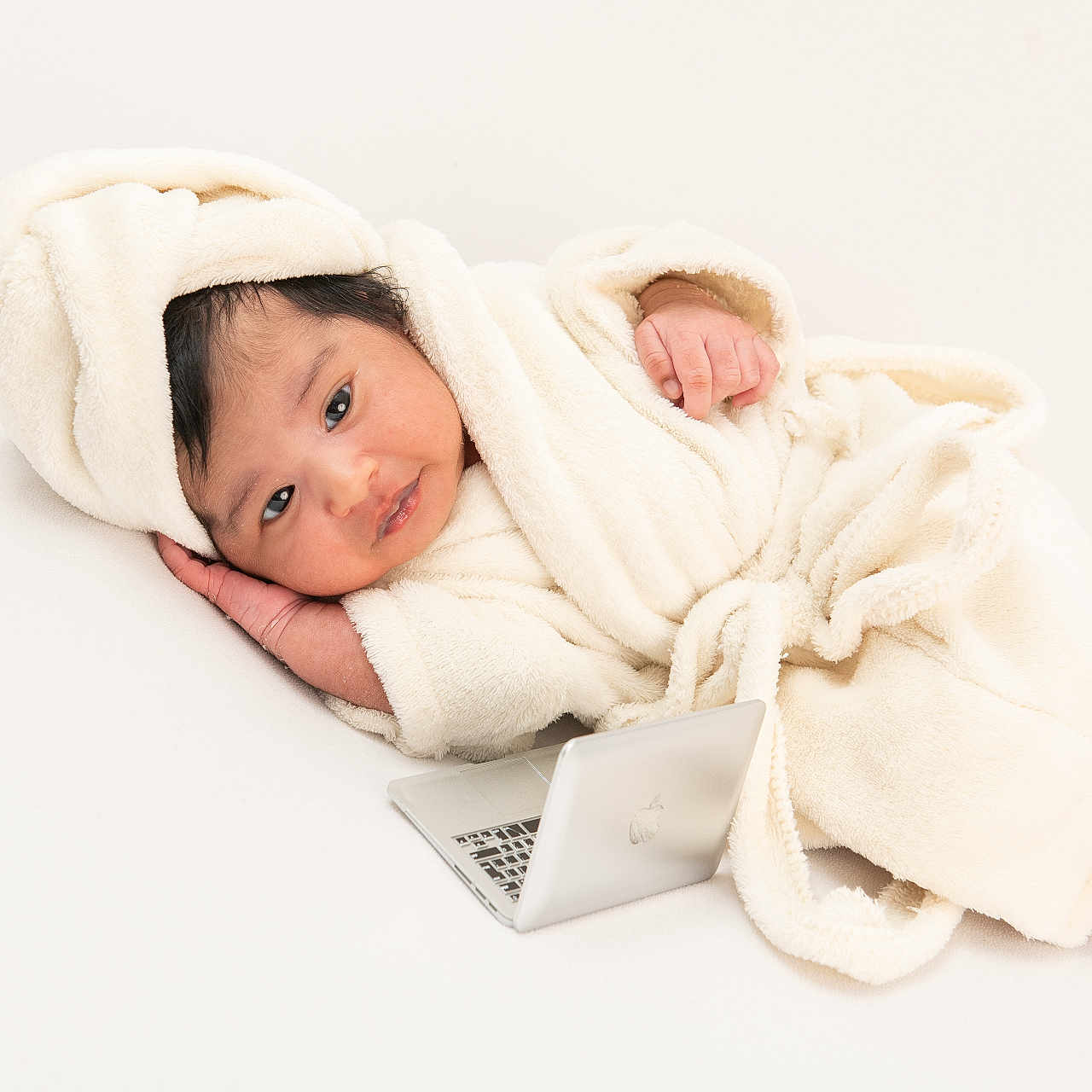 Aarya joined the competition — help win amazing prizes! baby, cozy, cute, eyes, face, fluffy, foot, hand, indoor, infant, laptop, lying_down, portrait, relaxed, robe, skin, small_object, soft_texture, technology, white_background