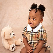 Amoura-Reign is registered to the contest to win money with this photo: baby, child, childhood, cute, earrings, fashion, happy, indoor, infant, kneeling, person, pigtails, plaid_clothing, portrait, smiling, soft_background, studio, teddy_bear, toddler, toy