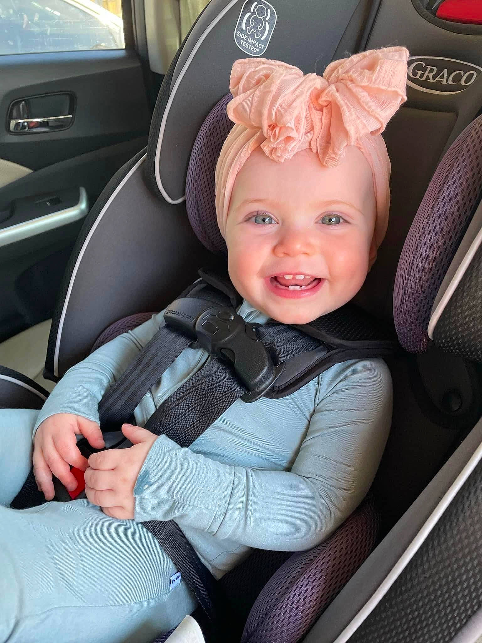 Molly is registered to the contest to win money with this photo: auto_part, automotive_design, automotive_exterior, baby, car, car_seat, car_seat_cover, clothing, comfort, head_restraint, headwear, motor_vehicle, person, plant, seat_belt, smile, steering_part, steering_wheel, toddler, vehicle
