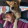 man, dog, car, window, smile, happy, casual_clothing, cap, pet, friendship, indoor, seat, seatbelt, urban_background, paw, fur, headwear, gesture, human, animal