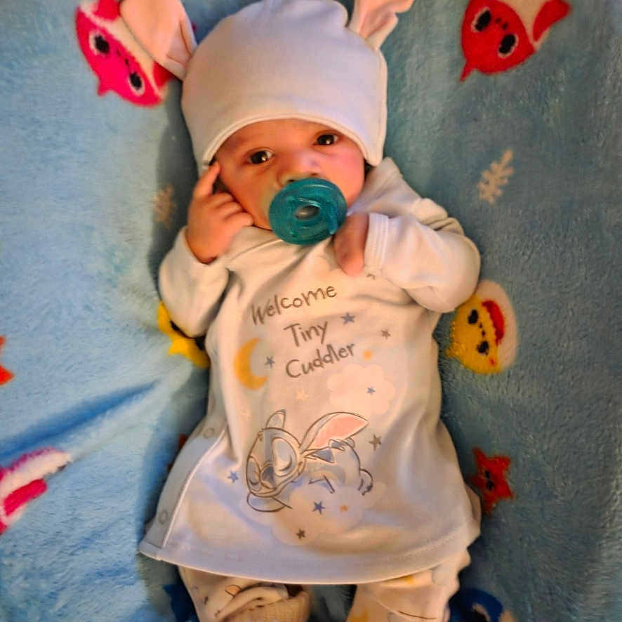 Daymeir is registered to the contest to win money with this photo: baby, baby_clothes, blanket, blue_blanket, booties, bunny, cartoon_print, cute, hat_with_bunny_ears, headwear, indoors, infant, lying_down, newborn, onesie, pacifier, portrait, sleepy, small_person, socks