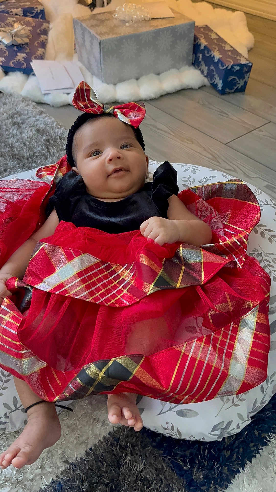 Sahani is registered to the contest to win money with this photo: baby, bow_headband, carpet, child, cushion, cute, festive, flooring, footwear_free, gift_boxes, happy, holiday_theme, indoor, infant, person, plaid_pattern, portrait, red_dress, smiling, toddler