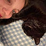 person, face, cat, black_cat, pet, sleeping, pillow, checkered_pattern, closeup, indoor, cozy, resting, companion, snuggling, cute, feline, human, portrait, relaxing, bedroom