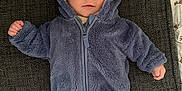 Ted is registered to the contest to win money with this photo: baby, child, infant, blue_jacket, hood, ears, couch, fabric, texture, person, clothing, cute, smile, face, eyes, indoor, laying_down, warm_clothing, cozy, small_hands