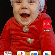 Diego participe au concours pour gagner de l'argent avec cette photo : baby, child, smiling, santa_hat, red_clothing, holiday_outfit, portrait, face, infant, festive, cute, happy, indoors, app_icons, smartphone_screen, google_search_bar, button, clothing, person, screen