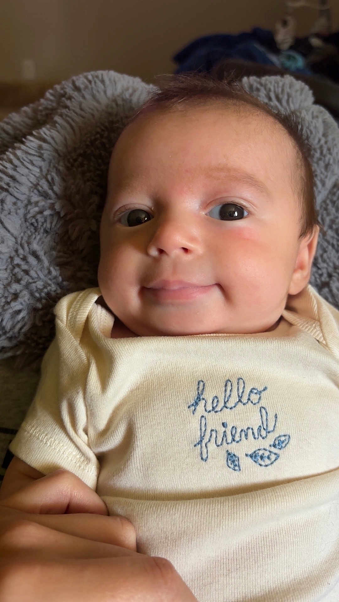 Clay is registered to the contest to win money with this photo: baby, infant, face, eyes, smile, hand, blanket, onesie, clothing, embroidery, text_on_clothing, skin, head, person, portrait, indoor, cute, young_child, human, cozy
