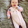 baby, child, infant, smiling, lying_down, pink_outfit, onesie, blanket, bed, indoor, portrait, face, hands, baby_clothing, butterfly_stickers, patterned_background, cozy, happy, photography, cute