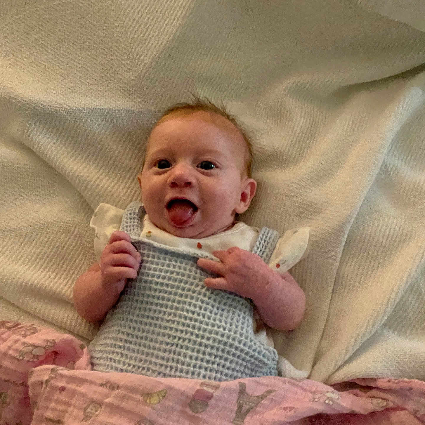 Hazel joined the competition — help win amazing prizes! baby, infant, blanket, knitted_clothing, smiling, tongue_out, lying_down, cute, happy, cozy, fabric, soft_texture, child, person, newborn, playful, indoors, warm, portrait, resting