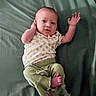 Hazel joined the competition — help win amazing prizes! baby, infant, child, cute, lying_down, green_bedspread, clothing, patterned_shirt, pants, hand, foot, face, skin, expression, looking_at_camera, indoors, portrait, relaxed, small_child, newborn
