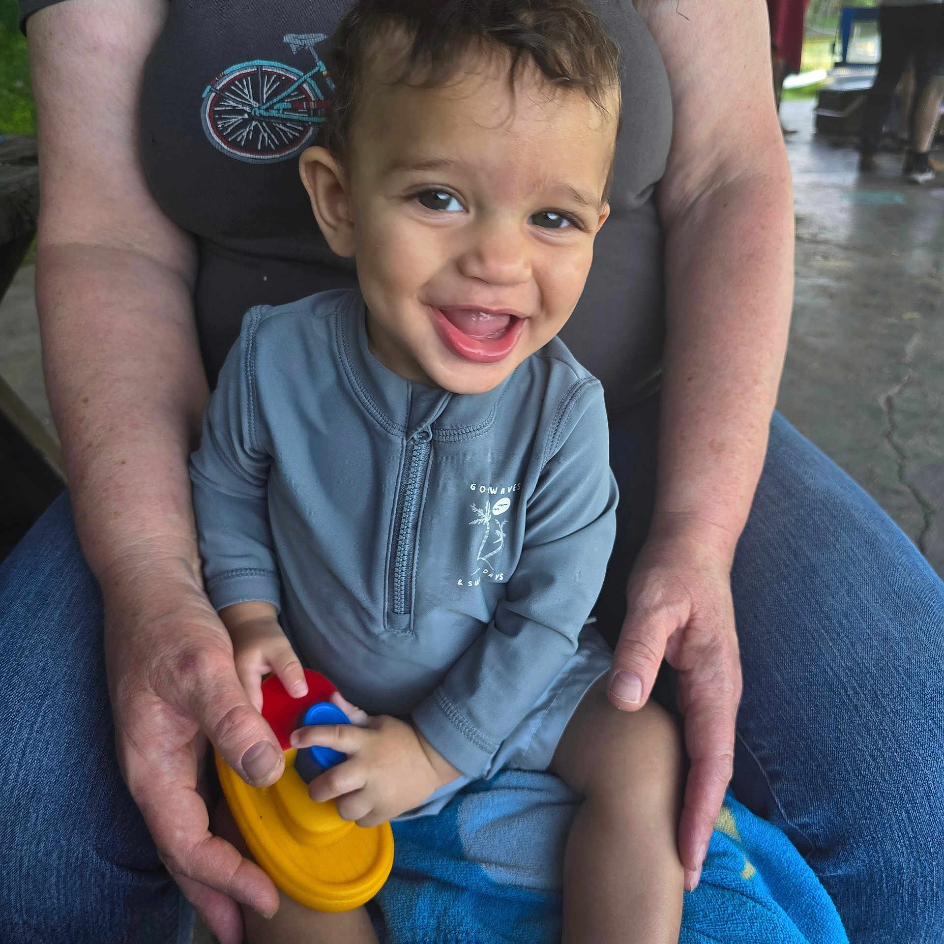 Noah joined the competition — help win amazing prizes! adult, boat, casual, child, clothing, concrete_floor, face, greenery, hands, happy, jeans, outdoor, person, play, portrait, shirt, sitting, smile, toddler, toy