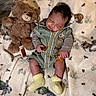 baby, teddy_bear, blanket, sleeping, infant, soft_toy, cute, child, cozy, yellow_socks, green_outfit, animal_print, bedtime, peaceful, indoors, plush, small_packets, resting, portrait, comfort