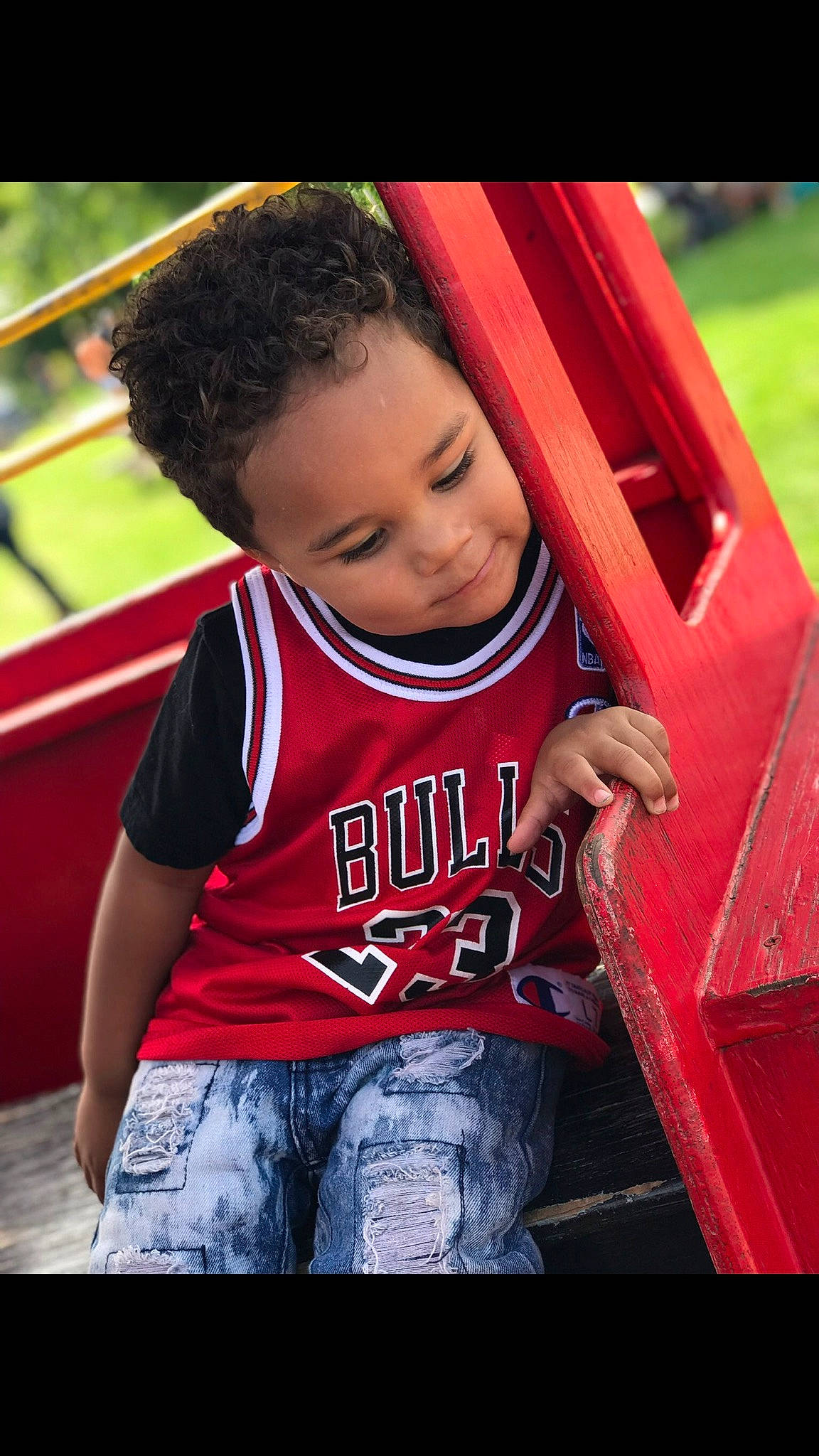 Davien is registered to the contest to win money with this photo: child, cool, facial_expression, flash_photography, fun, grass, happy, leisure, outdoor_play_equipment, person, playground, recreation, red, sitting, skin, smile, standing, t_shirt, tints_and_shades, toddler