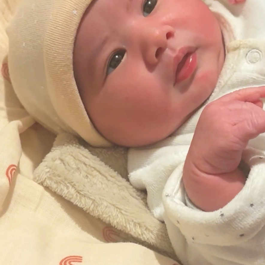 Alya participe au concours pour gagner de l'argent avec cette photo : baby, infant, hat, blanket, onesie, face, hand, cute, sleepwear, soft, patterned, cozy, newborn, gazing, skin, lying_down, indoors, portrait, child, peaceful