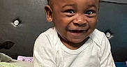 Ezekiel is registered to the contest to win money with this photo: bed, child, clothing, curtains, cute, face, hair, happy, headboard, home, indoor, joy, pants, person, portrait, seated, skin, smiling, toddler, white_shirt