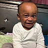 Ezekiel is registered to the contest to win money with this photo: toddler, child, smiling, happy, indoor, bed, clothing, white_shirt, pants, face, person, curtains, headboard, home, seated, cute, portrait, skin, hair, joy