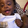 Ezekiel is registered to the contest to win money with this photo: baby, child, person, face, smile, leopard_print, tattoo, clothing, hand, indoor, arm, white_shirt, joyful, motion_blur, portrait, cute, skin, expression, holding, infant