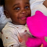 Ezekiel is registered to the contest to win money with this photo: toddler, child, smile, happy, plush_toy, pink_toy, person, baby, clothing, white_shirt, indoor, cute, portrait, hand, face, sitting, joyful, young_child, holding, toy