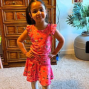 Aiza Grenevitch is registered to the contest to win money with this photo: child, girl, portrait, standing, smiling, dress, floral_pattern, coral_color, hands_on_hips, indoors, home, bedroom, dresser, wooden_furniture, houseplant, framed_photos, carpet, fashion, full_body, family_photo