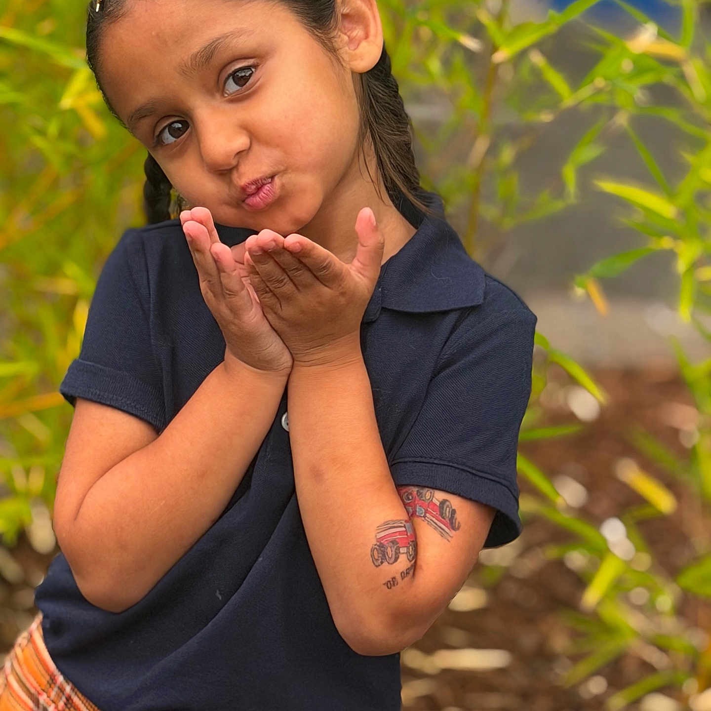 Aiza Grenevitch joined the competition — help win amazing prizes! child, portrait, outdoor, smiling, playful, blowing_kiss, face, eyes, hair, hair_accessory, hands, arms, shirt, plaid_clothing, short_sleeves, tattoo, greenery, plants, garden, bokeh