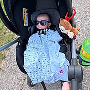 Brayden joined the competition — help win amazing prizes! baby, stroller, sunglasses, blanket, plush_toy, outdoor, pavement, hand, greenery, toy, person, infant, clothing, sunlight, footwear, parent, accessory, shade, cute, relaxation
