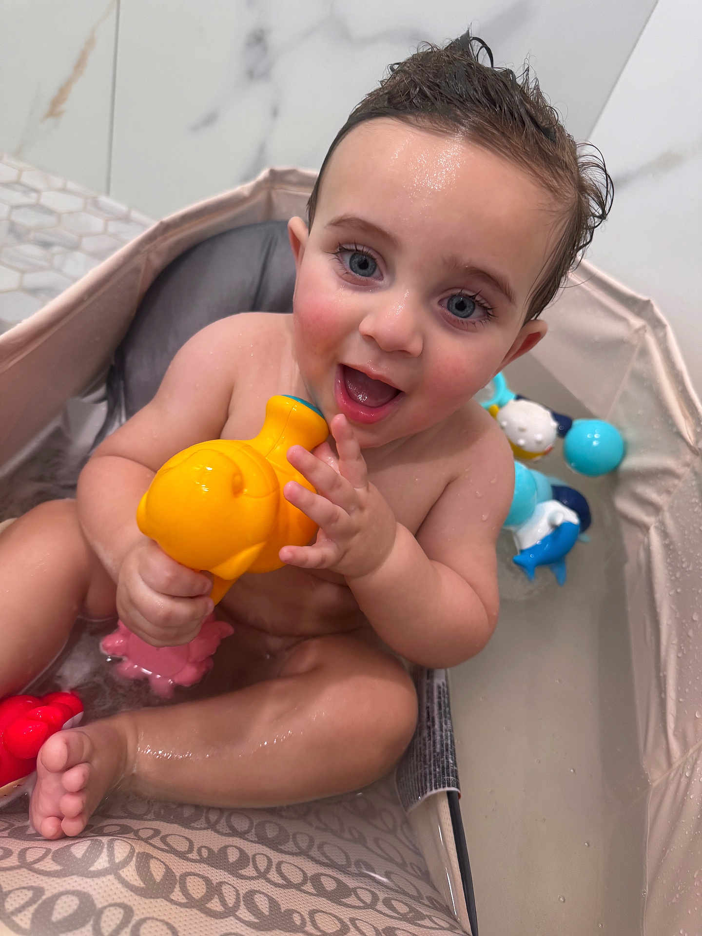 Youssuf joined the competition — help win amazing prizes! baby, bath_seat, bath_time, bathtub, blue_eyes, child, close_up, foot, hand, infant, marble_wall, plastic_toy, sitting, skin, smile, splash, toy, water, wet_hair, yellow_toy