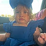 Kylie is registered to the contest to win money with this photo: child, toddler, portrait, car, vehicle, blue_dress, bow, hair, face, eyes, serious_expression, sitting, indoors, sunlight, window, passenger, adult_hand, seat, fashion, photography