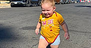 Kylie is registered to the contest to win money with this photo: child, toddler, girl, smiling, outdoor, street, sunny, daylight, yellow_shirt, sports_shirt, iowa_state, shorts, sandals, pigtails, standing, walking, parked_cars, pickup_truck, palm_trees, residential_neighborhood