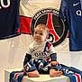Liam participe au concours pour gagner de l'argent avec cette photo : baby, barefoot, casual, child, clothing, curious, flag, football, indoor, logo, pedestal, person, portrait, psg_jersey, scarf, sitting, sports_fan, team_spirit, wall_hanging, young_child