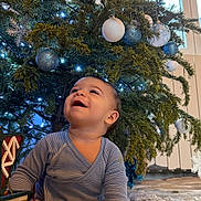 Liam a rejoint le concours — aidez-le/la à gagner de superbes lots ! baby, blue_ornaments, celebration, child, christmas_tree, cute, decorations, festive, floor, happy, holiday, indoor, lights, ornaments, pajamas, seasonal, smiling, socks, toy_house, white_ornaments