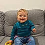 Lyna participe au concours pour gagner de l'argent avec cette photo : toddler, child, smiling, toy, yellow_ring, jeans, long_sleeve_shirt, teal_shirt, indoor, sofa, gray_couch, happy, playful, casual_clothing, cute, portrait, seated, young_child, home, person
