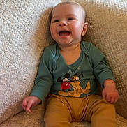 Atlas is registered to the contest to win money with this photo: baby, child, smiling, sitting, armchair, clothing, blue_socks, beige, indoor, happy, person, cute, plush, mickey_mouse, pluto, infant, cozy, portrait, young_child, furniture